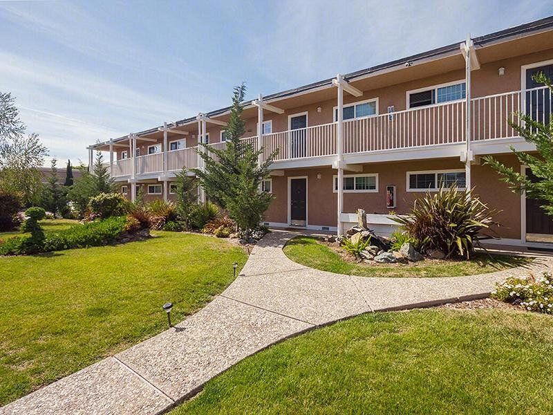 Two-story apartment building exterior with a landscaped lawn and curved walkway.