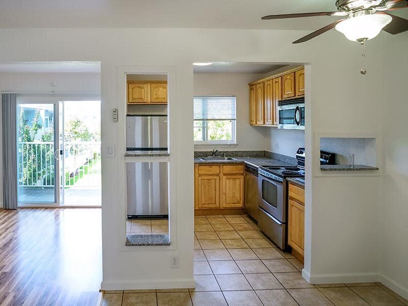 Open kitchen with stainless appliances and living area with balcony door.