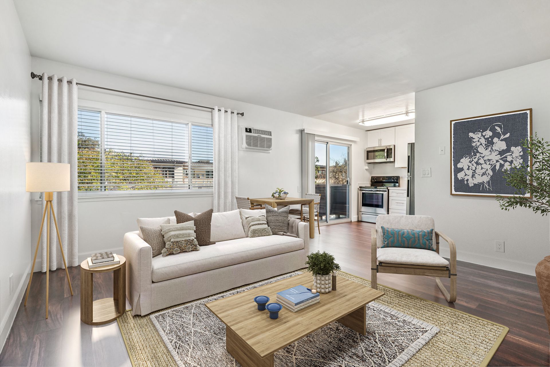 Living room with couch, coffee table, and open to kitchen; natural light and neutral tones.