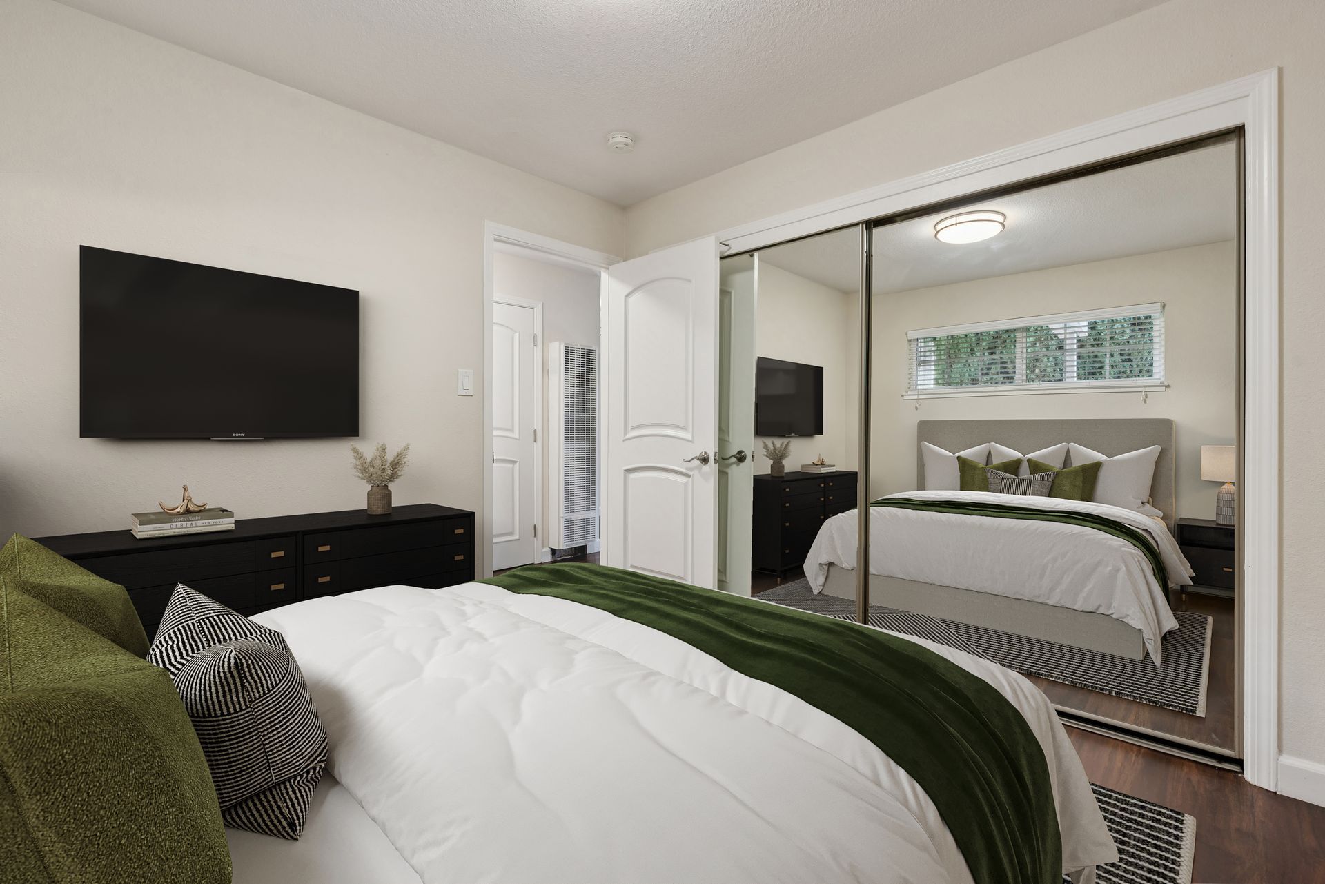 Bedroom with a bed, dresser, and a mirrored closet reflecting the room. Green accents.