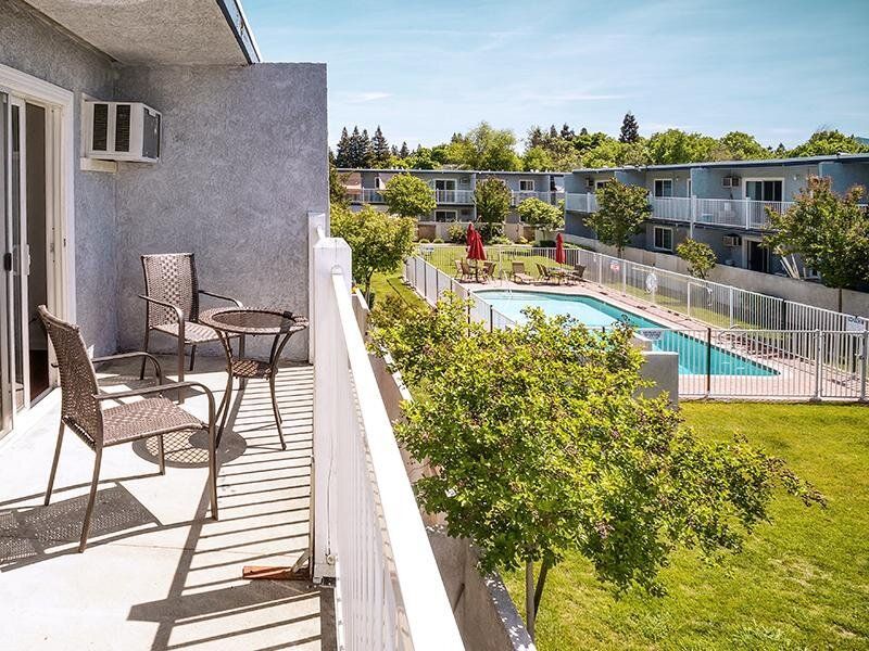 Balcony with wicker chairs and a small table overlooking a community pool and courtyard.