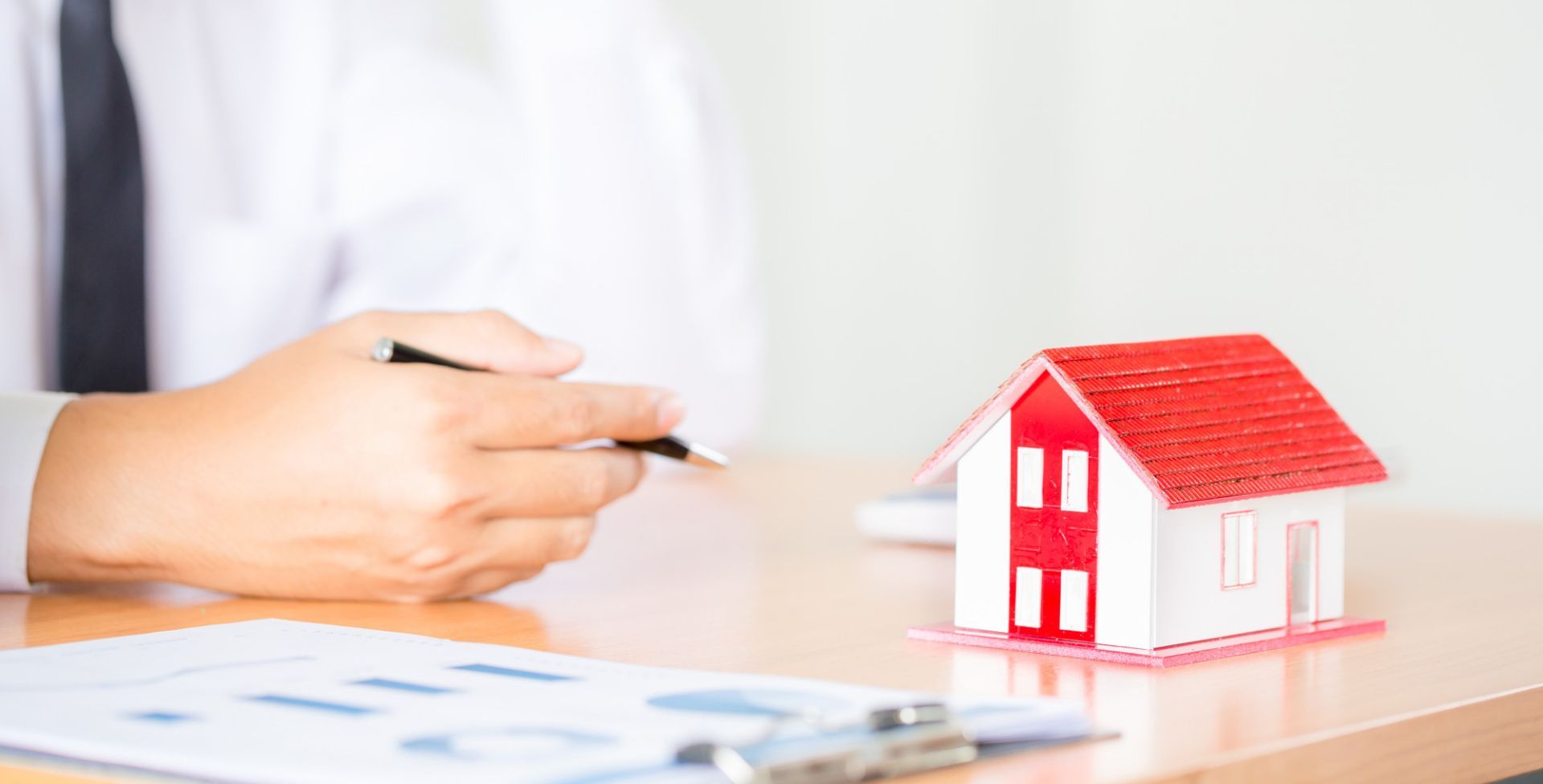 Man holding pen, looking at real estate documents with a toy house on a desk.