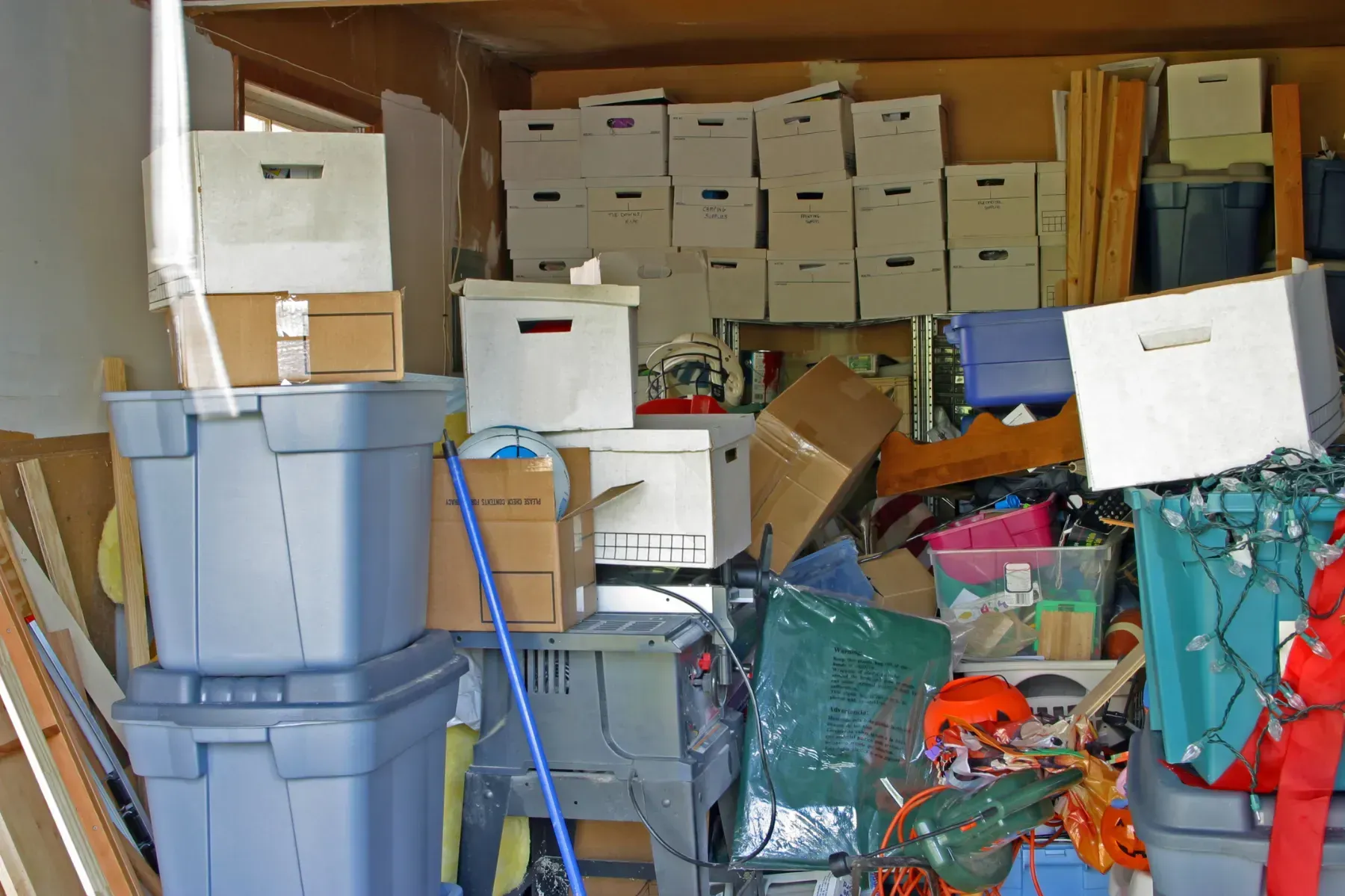 Cluttered garage with stacked boxes and bins filled with various items.