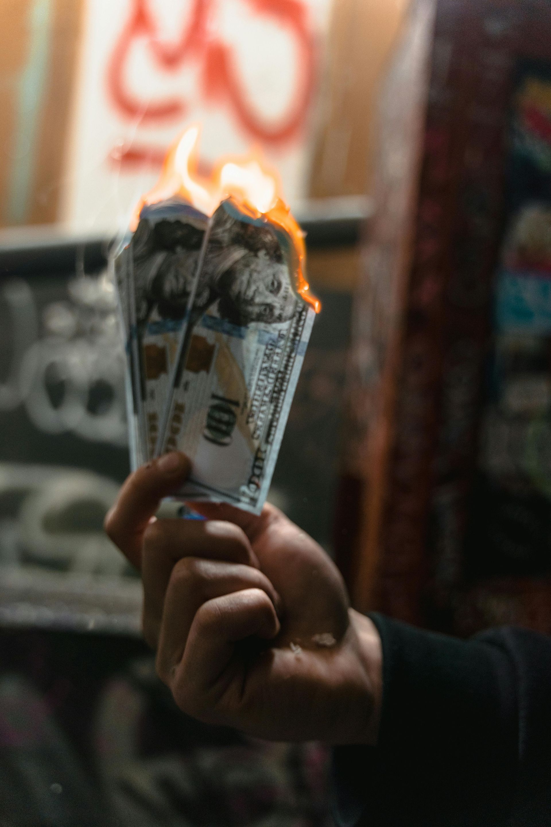 Hand holding burning hundred dollar bills. Graffiti backdrop.