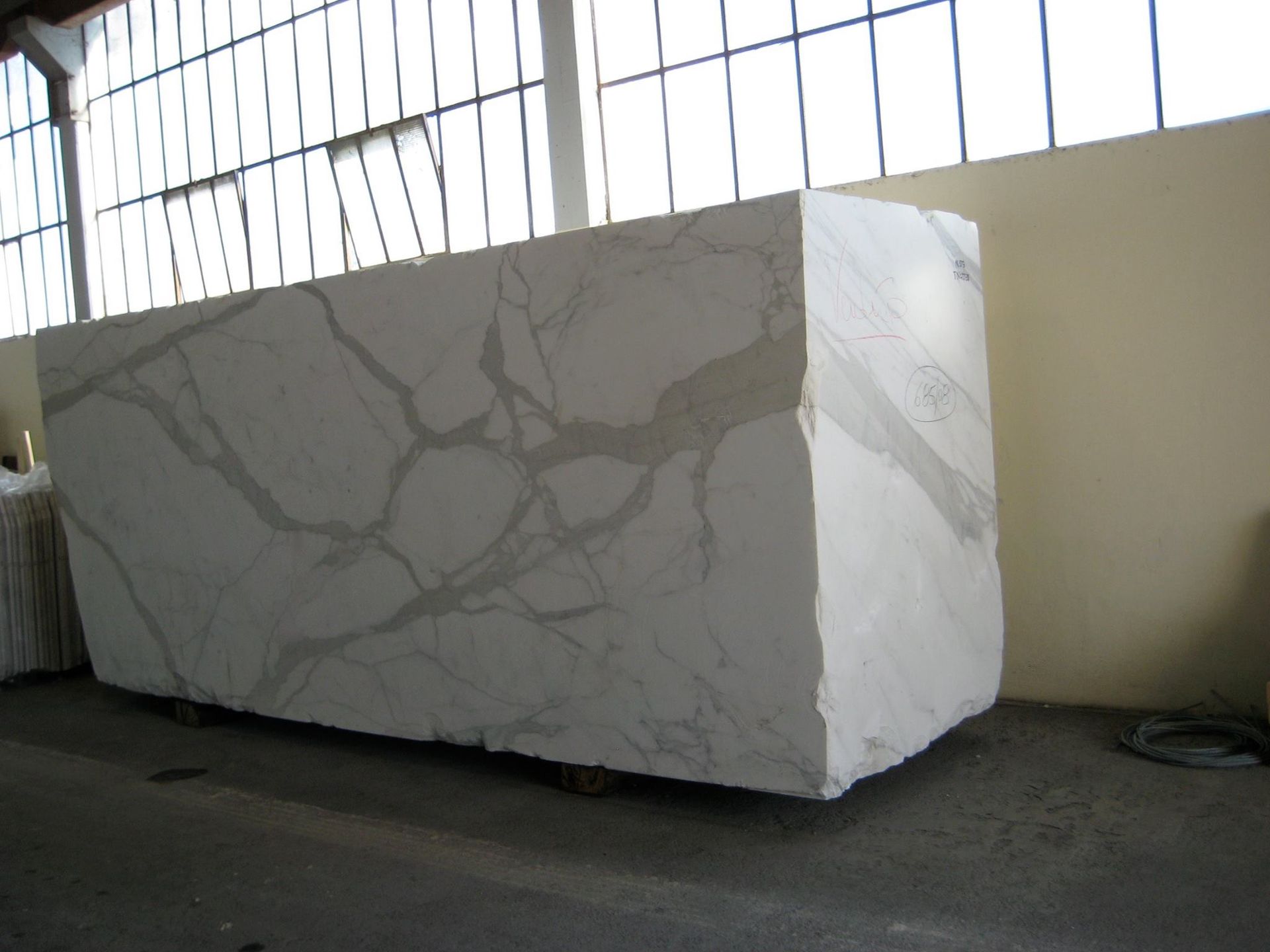 A large, white marble block with gray veining sits indoors, in a warehouse-like setting.