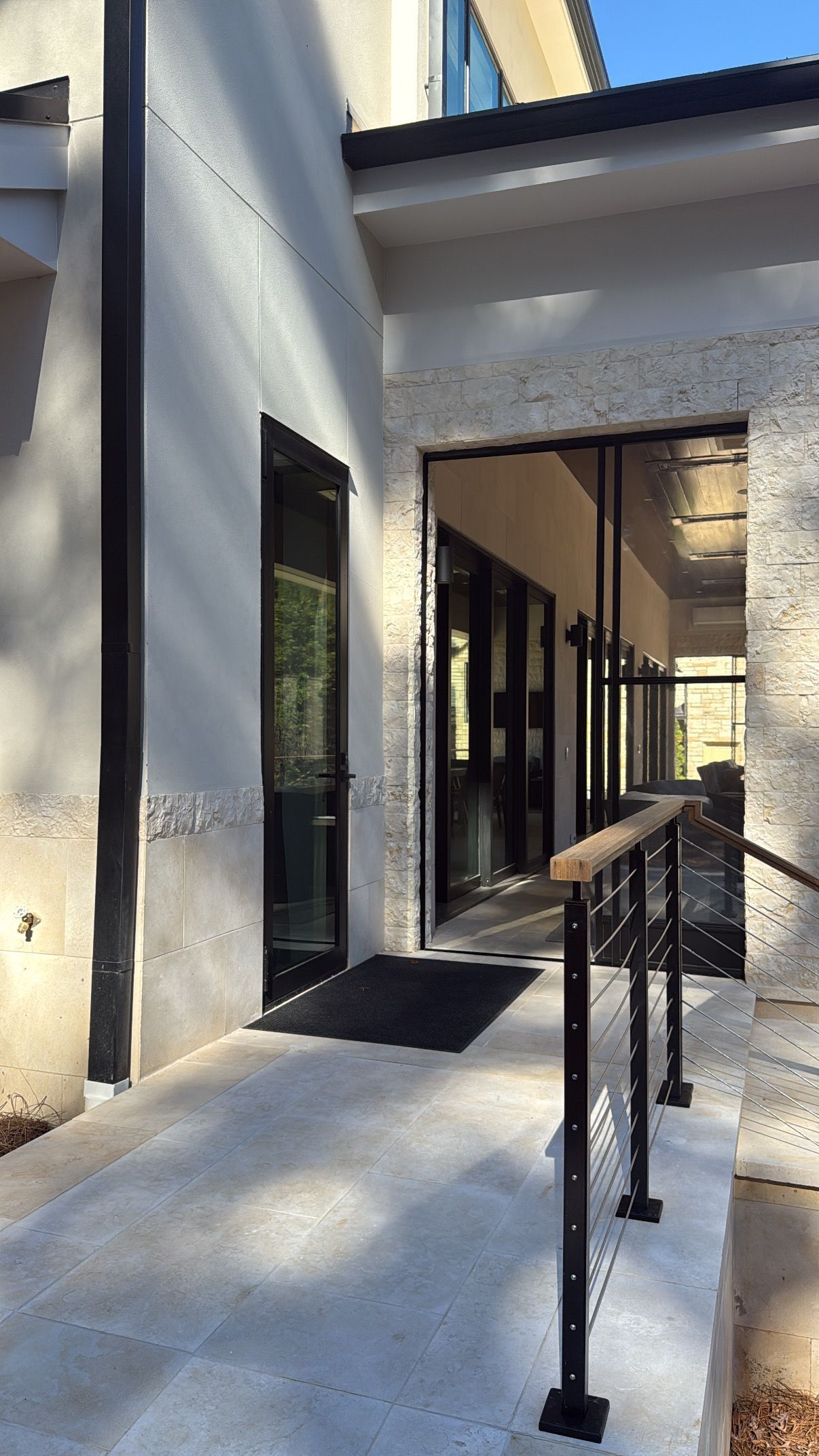 Exterior view of building entrance with ramp, black door, and handrail. White and gray stone.