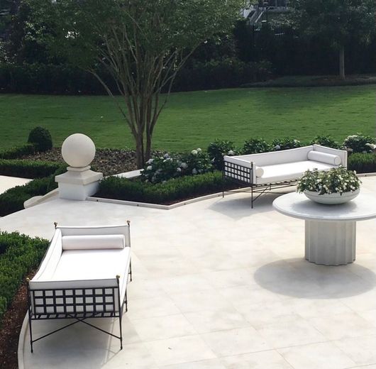 Patio with white furniture, manicured lawn, and a round marble table in a garden setting.