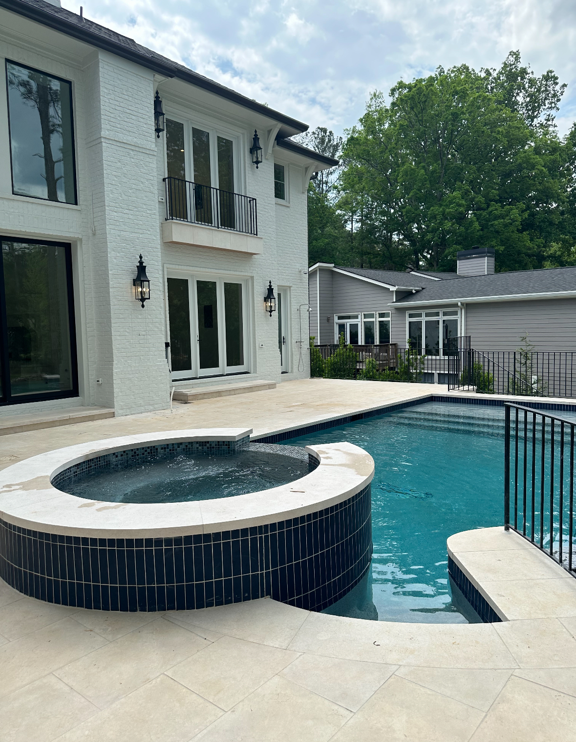 A luxury home with pool and spa. White textured facade, black trim, dark blue pool water.