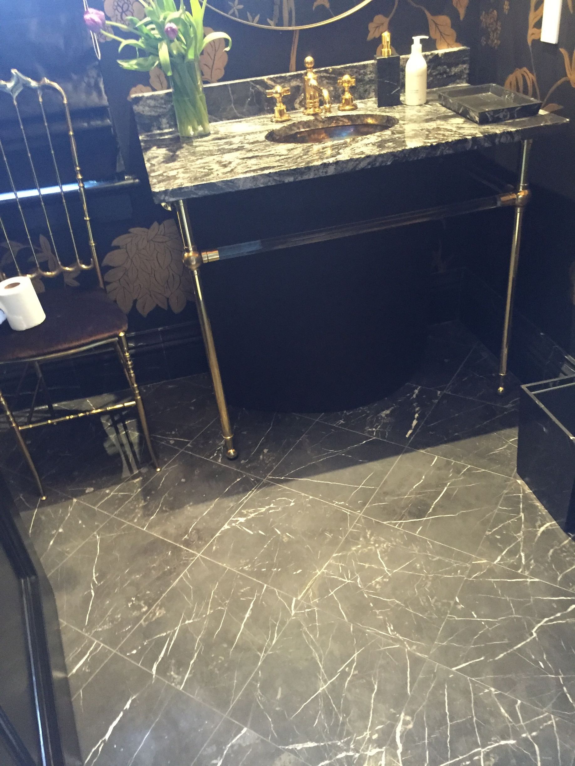 Bathroom with a black countertop, gold fixtures, and patterned dark floor.