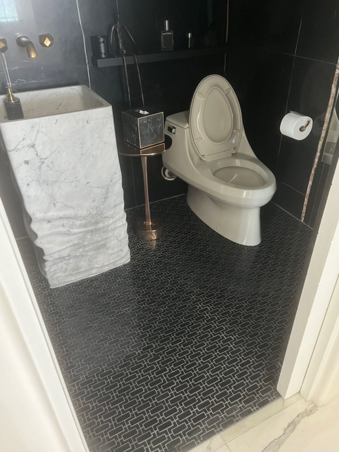 Black and white tiled bathroom with a pedestal sink, toilet, and gold accents.