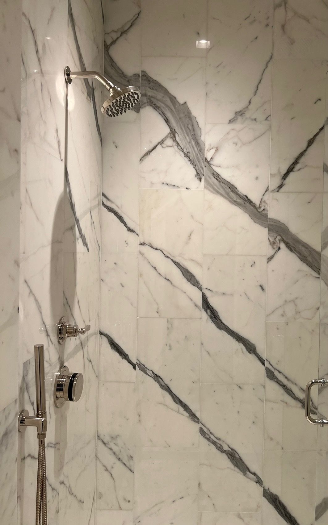 Shower with white marble walls and gray veining, chrome fixtures.