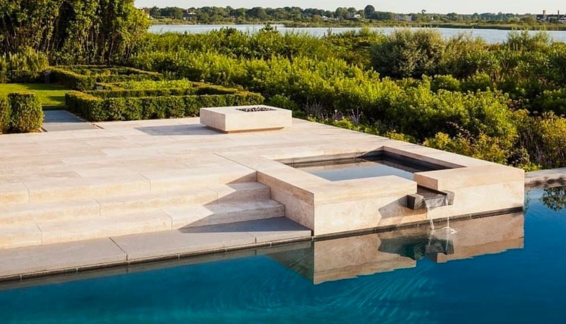 Outdoor pool with stone patio, small hot tub, and green foliage in the background.