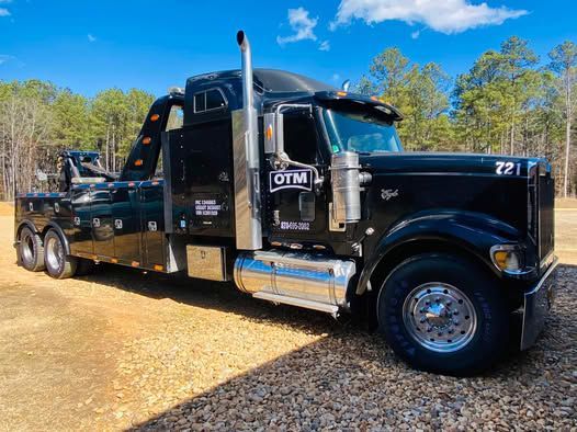 A black tow truck is parked in a gravel lot.