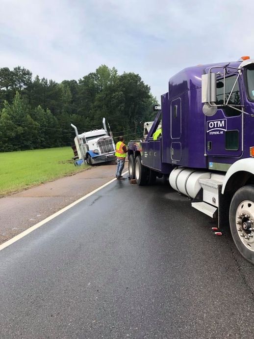 A purple tow truck is towing a white truck on the side of the road.