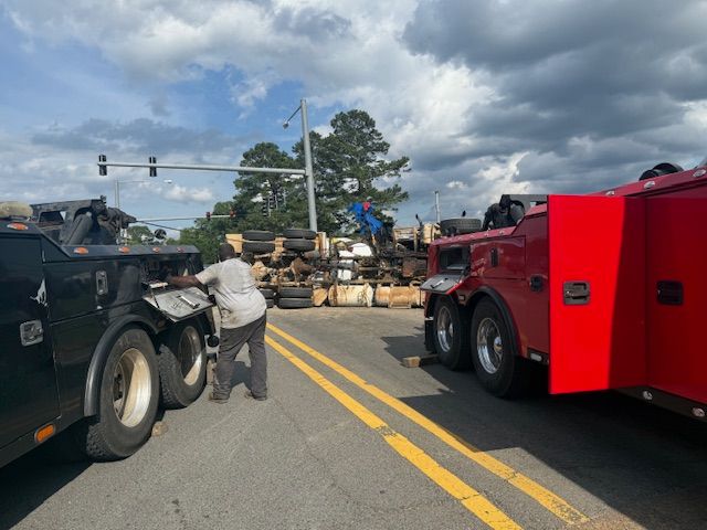 A purple tow truck is towing a white truck on the side of the road.