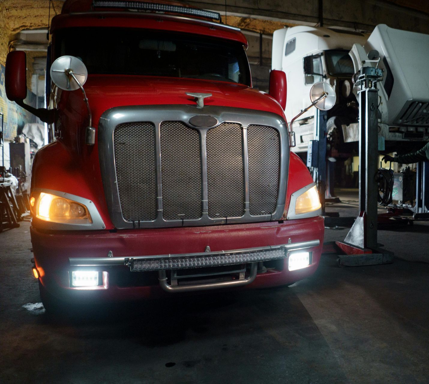 A red truck is parked in a garage with its lights on