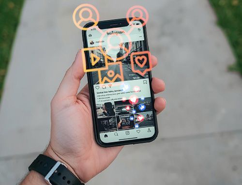 hand holding mobile phone with social media reactions floating over top of screen