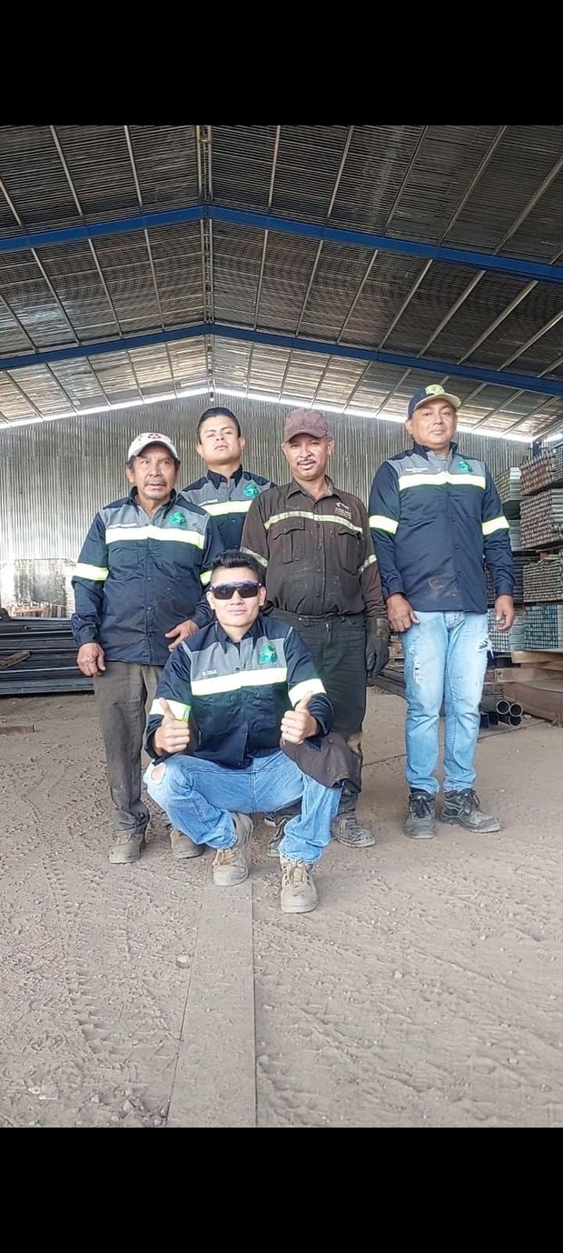 Cinco trabajadores con uniformes idénticos de color azul marino y gris posan dentro de una gran estructura de almacén de chapa ondulada.