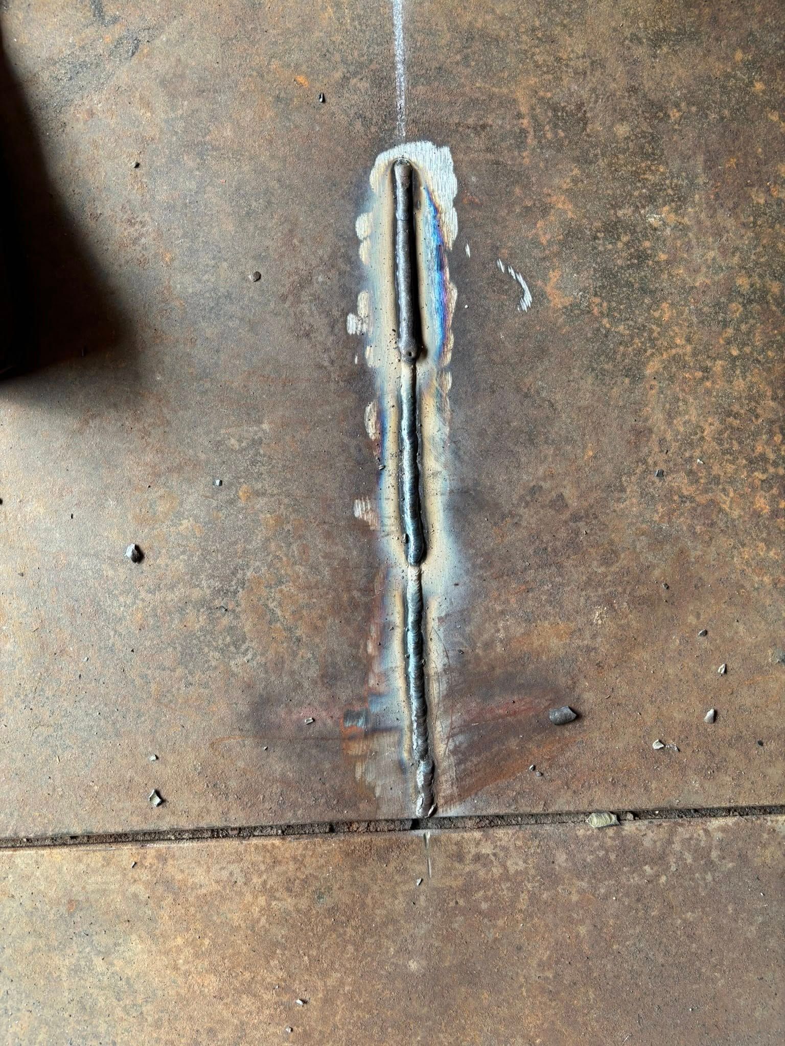 Welded seam on rusty metal surface, three weld beads visible in a straight line.