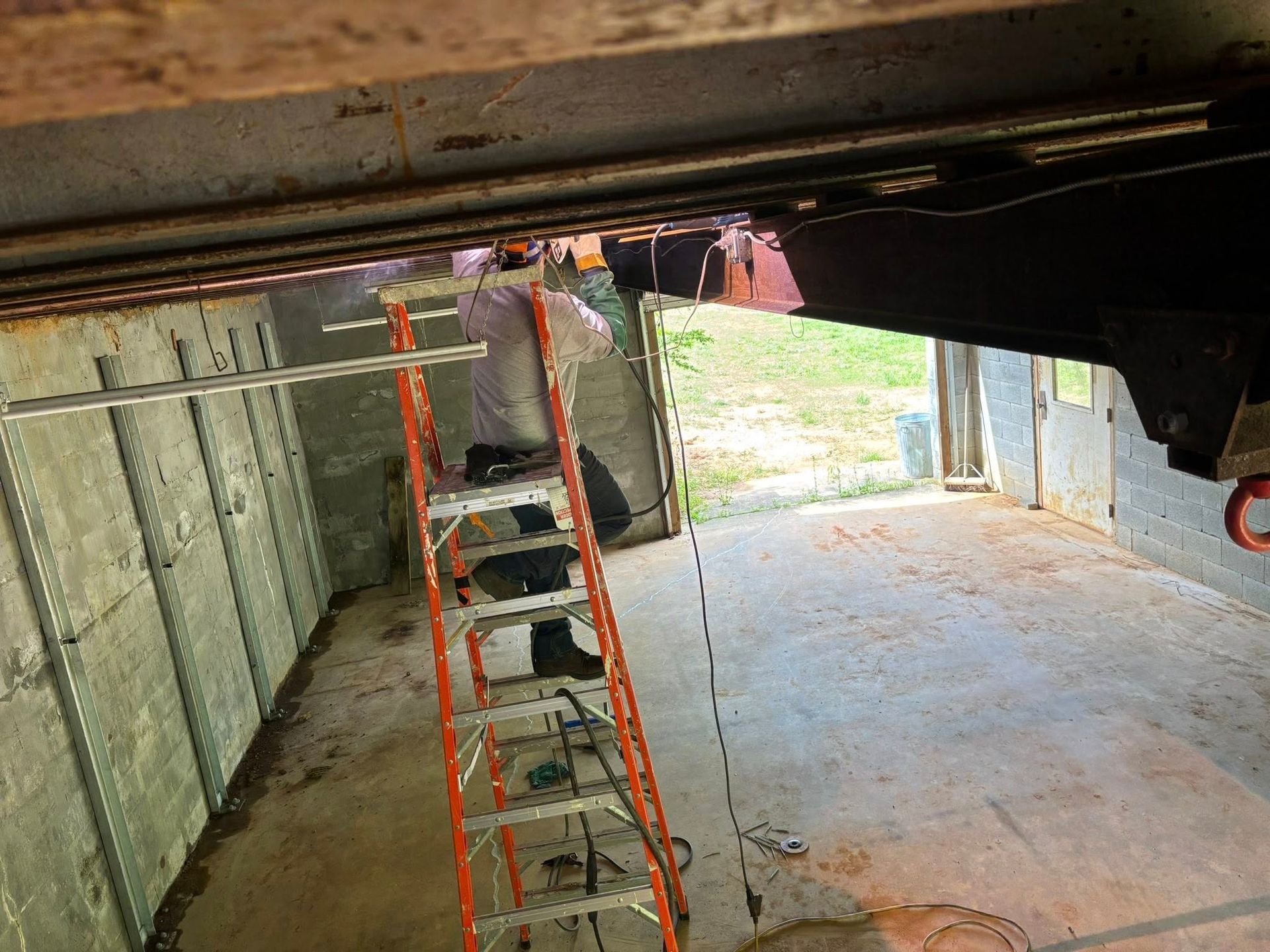 Person on ladder welding inside metal structure; open doorway to exterior.