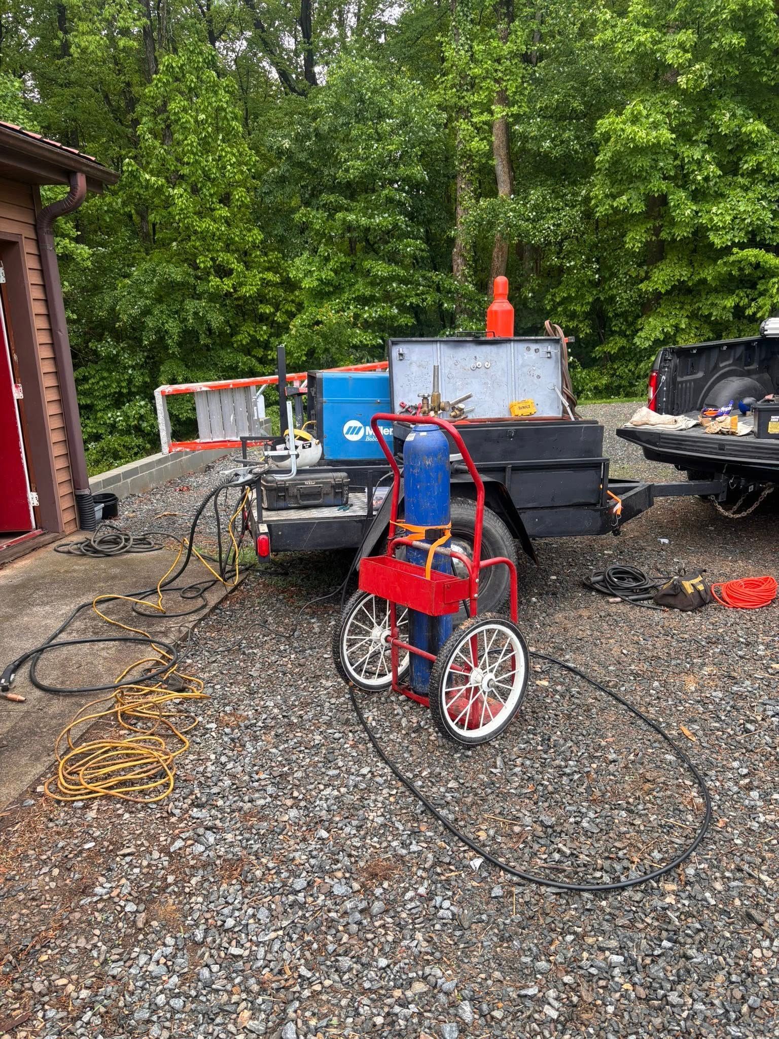 A welding rig on a trailer, with a blue oxygen tank and red cart.