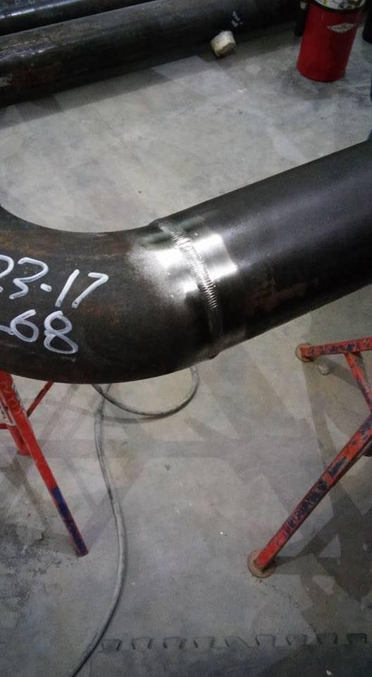 Steel pipe welded at a 90-degree angle, with visible welding seams and markings on the pipe.