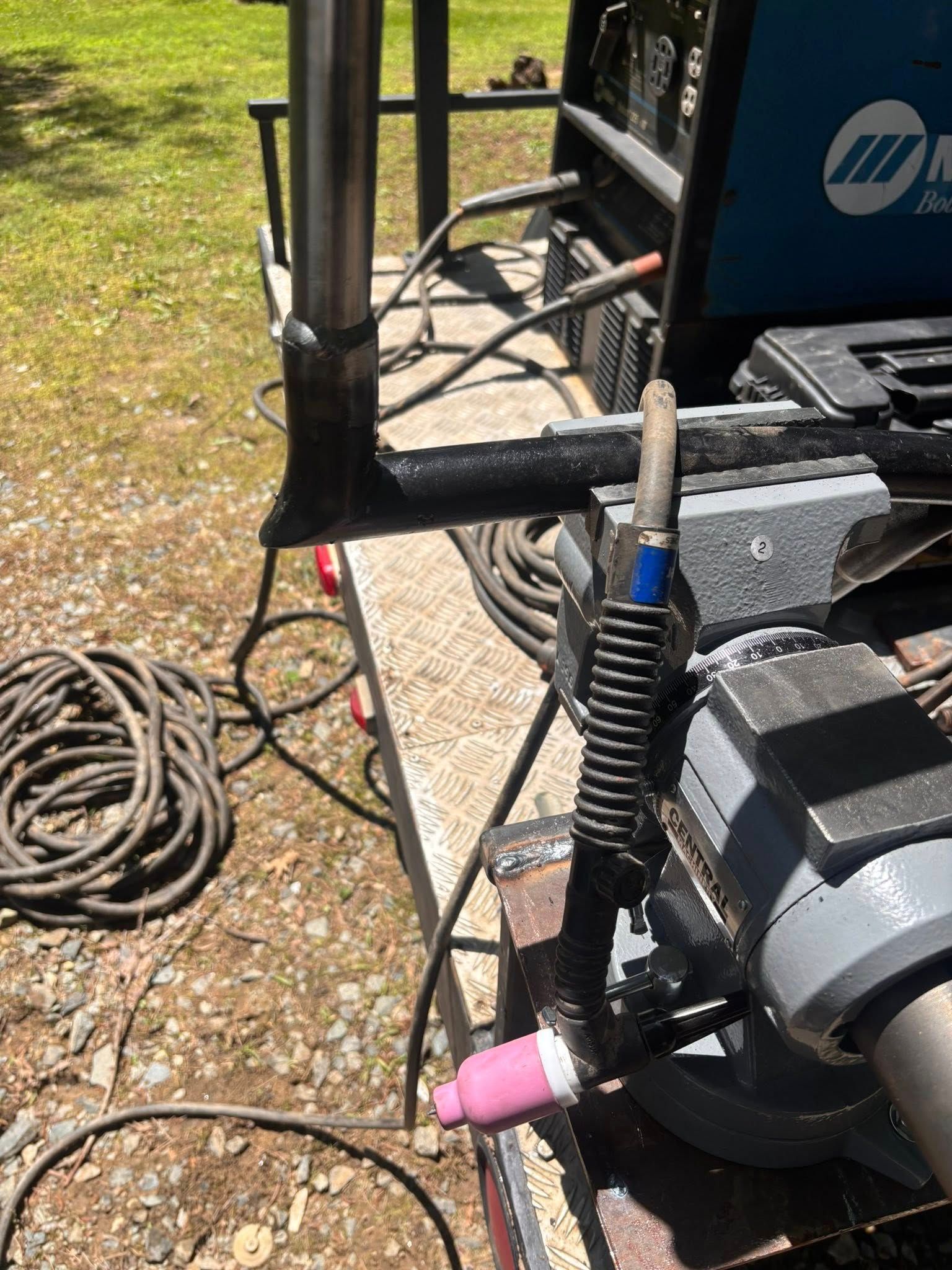 Welding equipment set up on a work surface, with a TIG torch and welded metal frame.