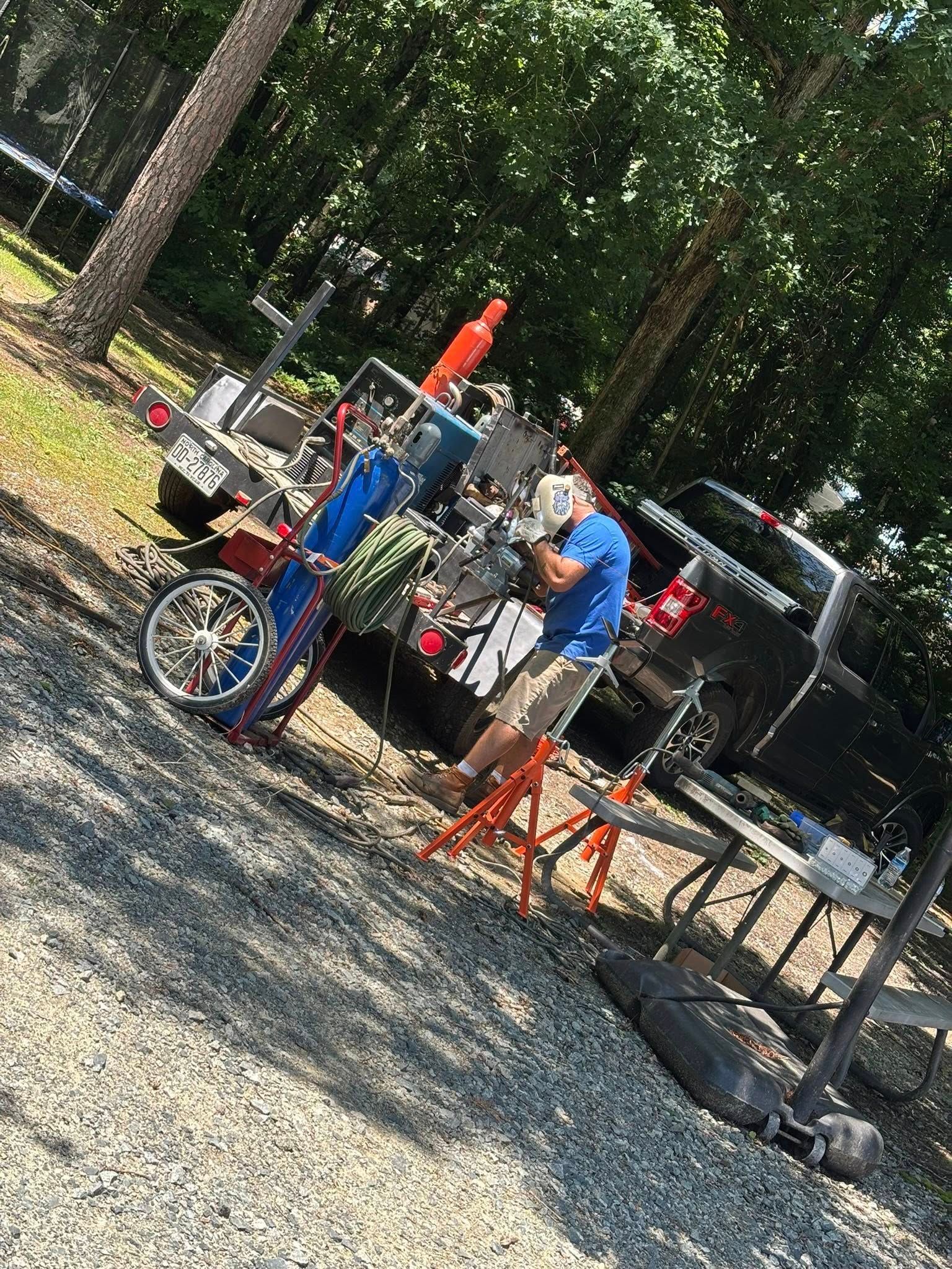 Man working on equipment attached to a trailer in a sunny, outdoor setting.