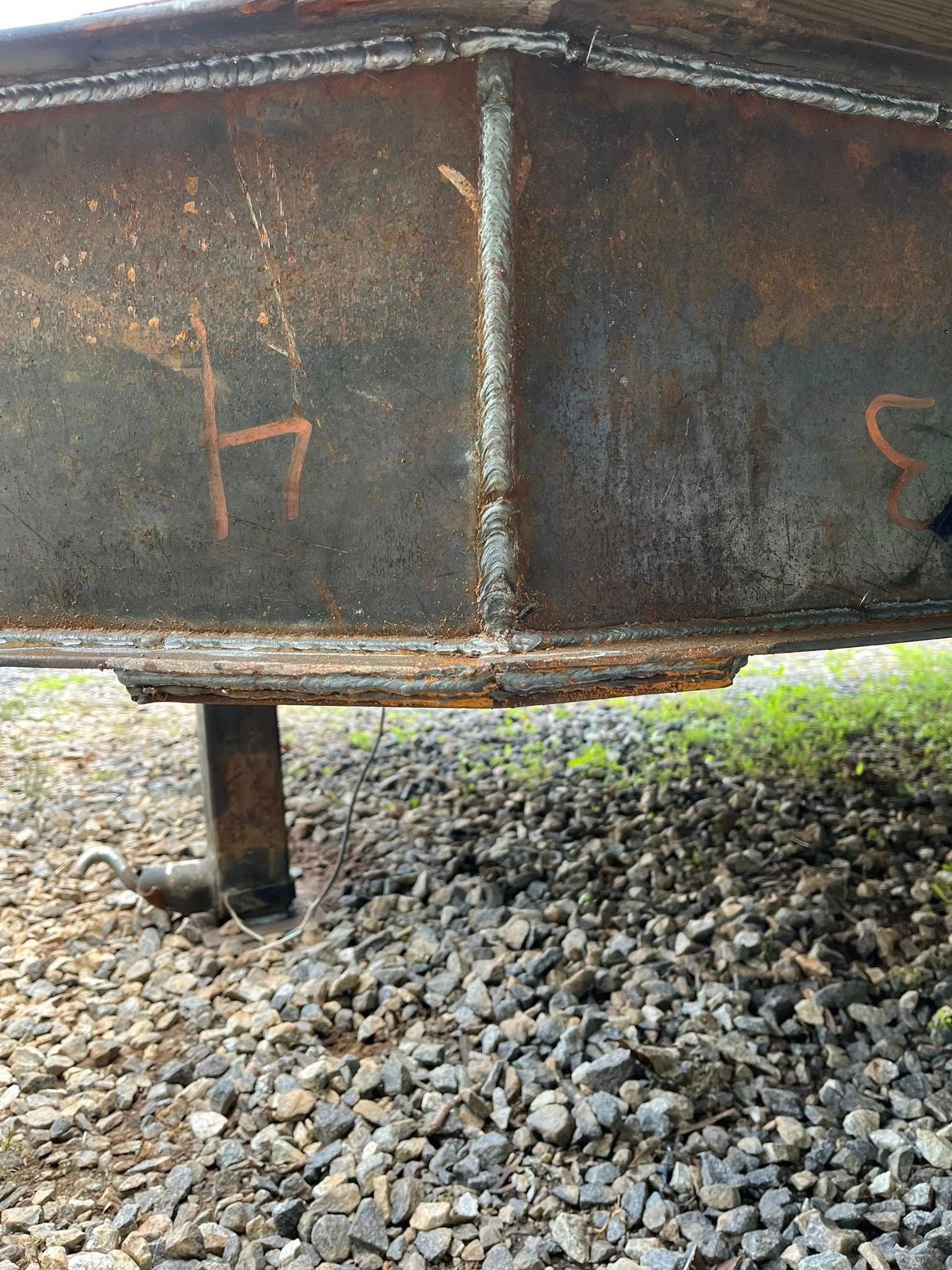 Rusty metal beam supported by a pillar, sitting above gravel and greenery.