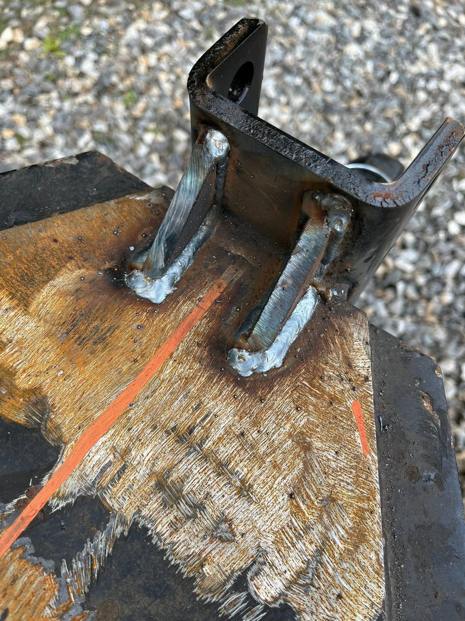 Black metal bracket welded to a worn, rusty surface, showing welding beads.