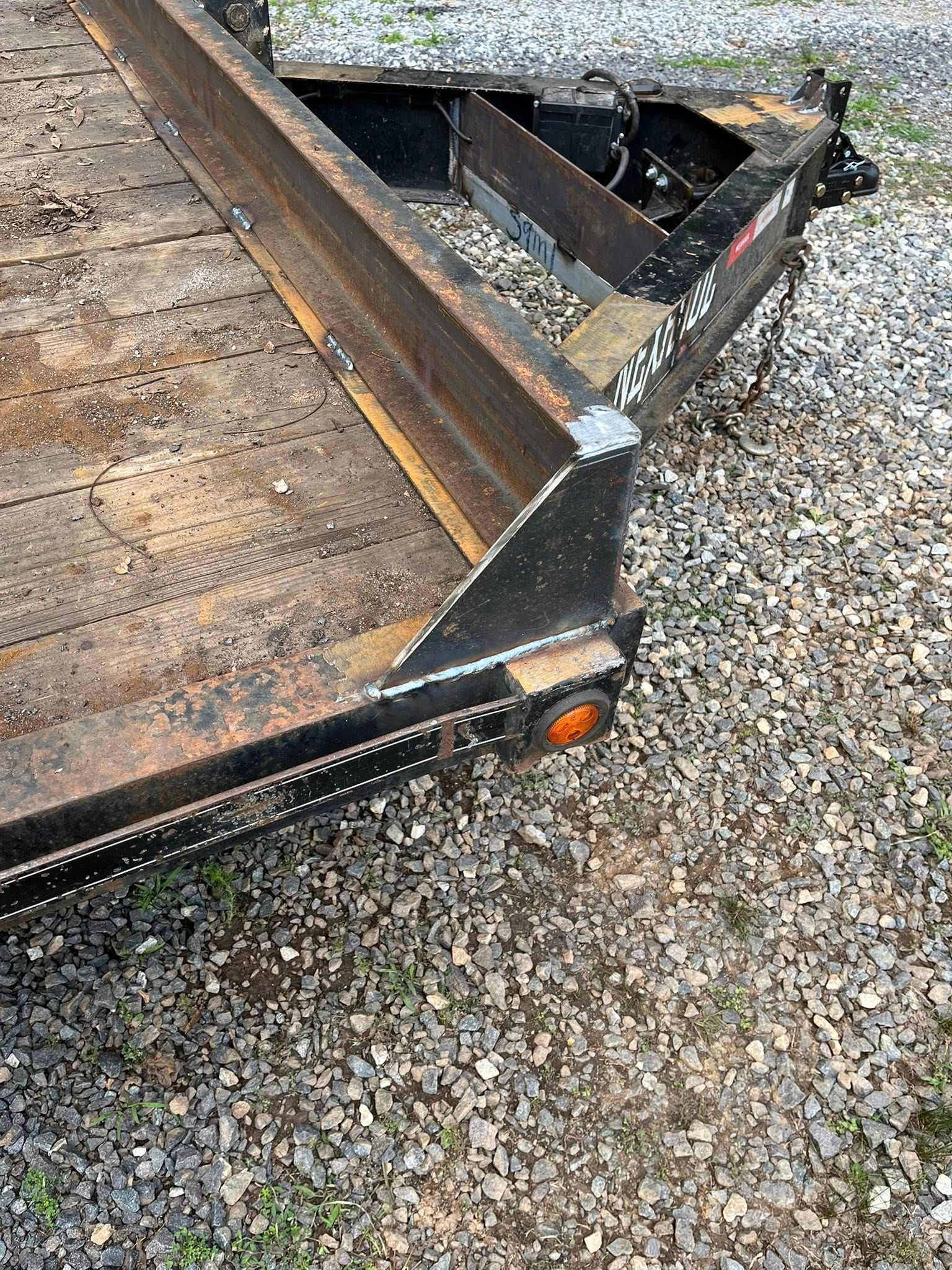 Black, rusty trailer on a gravel surface. Orange marker light visible.
