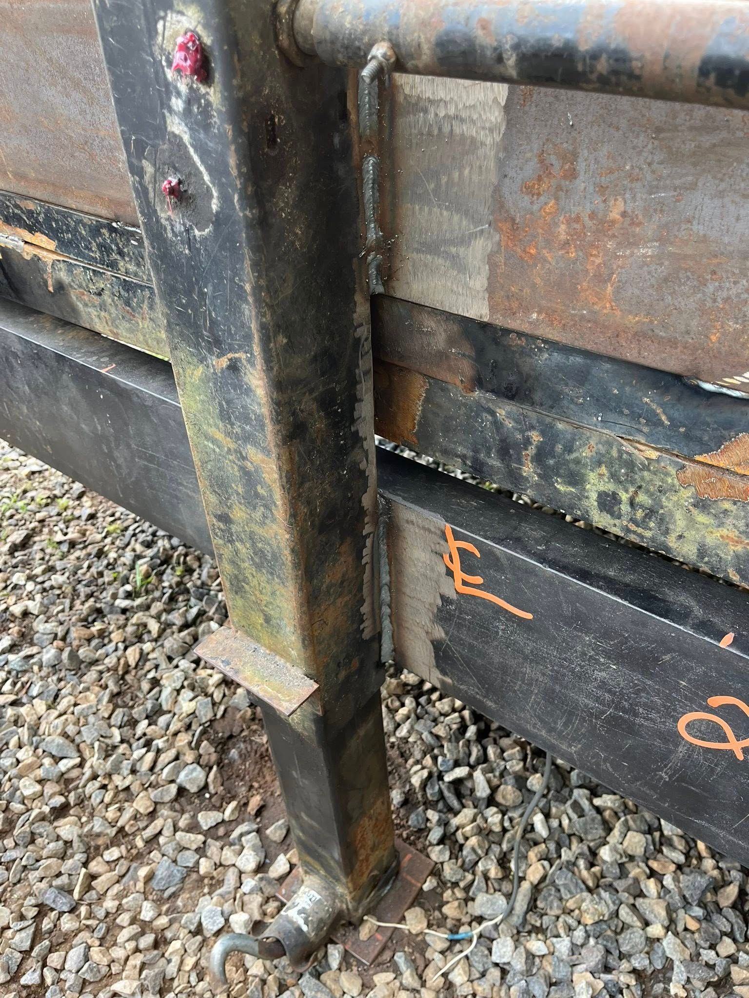 Close-up of a rusty metal trailer hitch. A black vertical support is visible next to the trailer bed.
