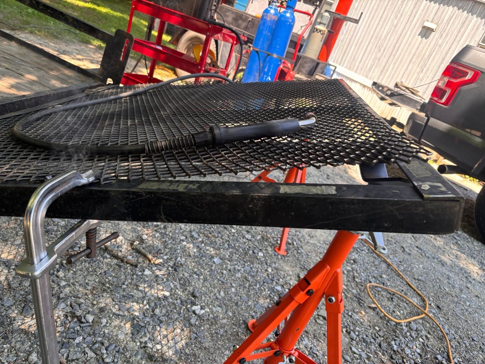 Welding table with mesh top, orange sawhorse supports, welding equipment, and a pickup truck.