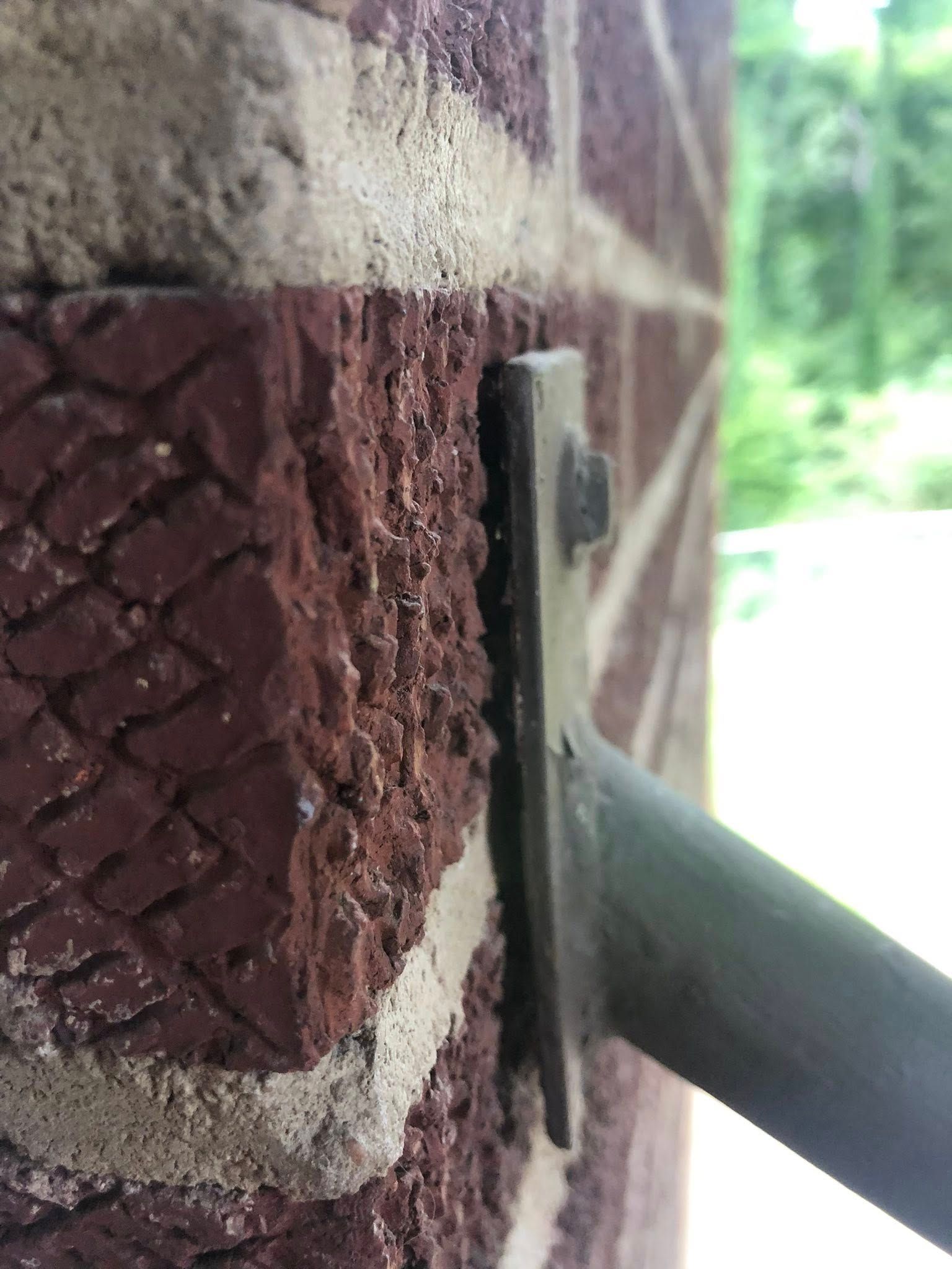 Metal bracket attached to a red brick wall with a bolt, supporting a metal pole.