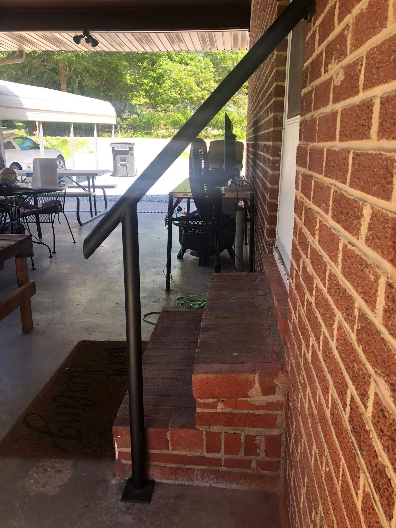 Dark gray sliding gate between two concrete pillars on a paved driveway with trees in the background.