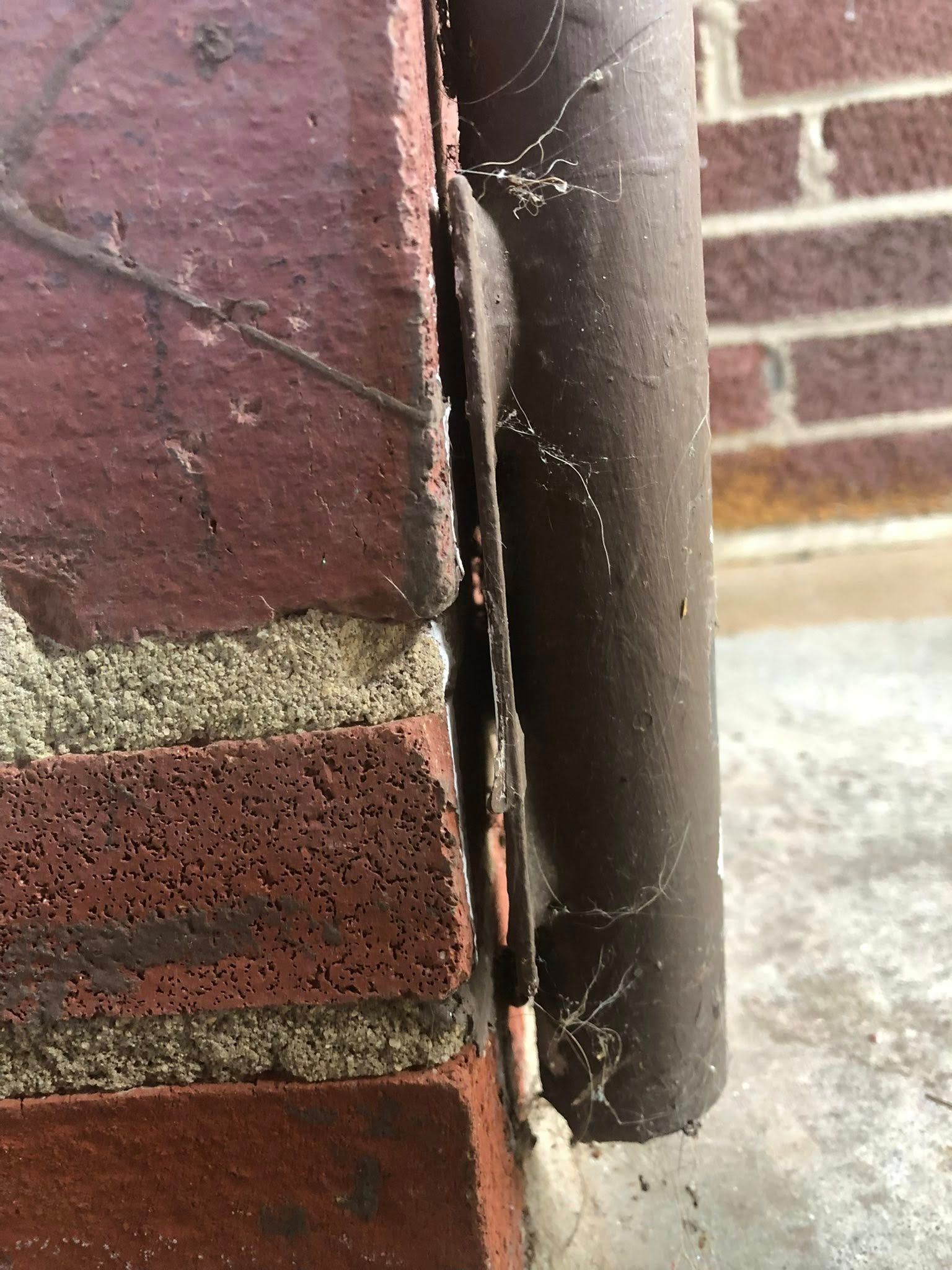 Brick wall with a dark metal pipe and a narrow gap.