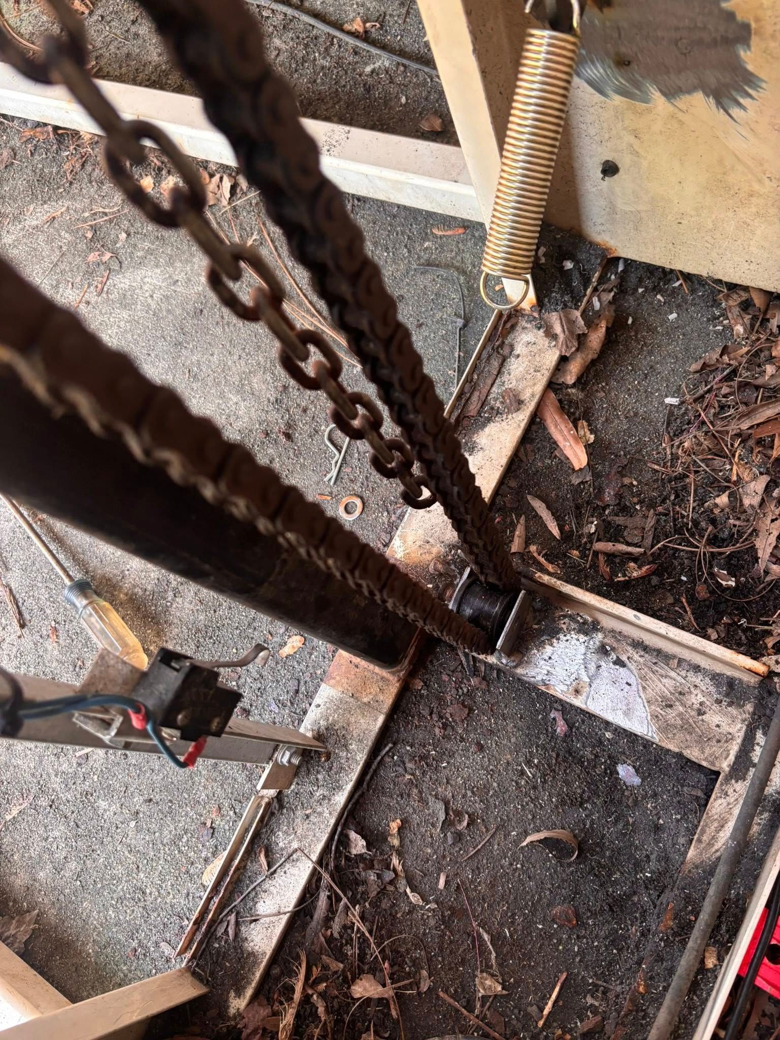 Overhead view of a rusty metal structure with a chain and a spring, possibly a mechanical component.