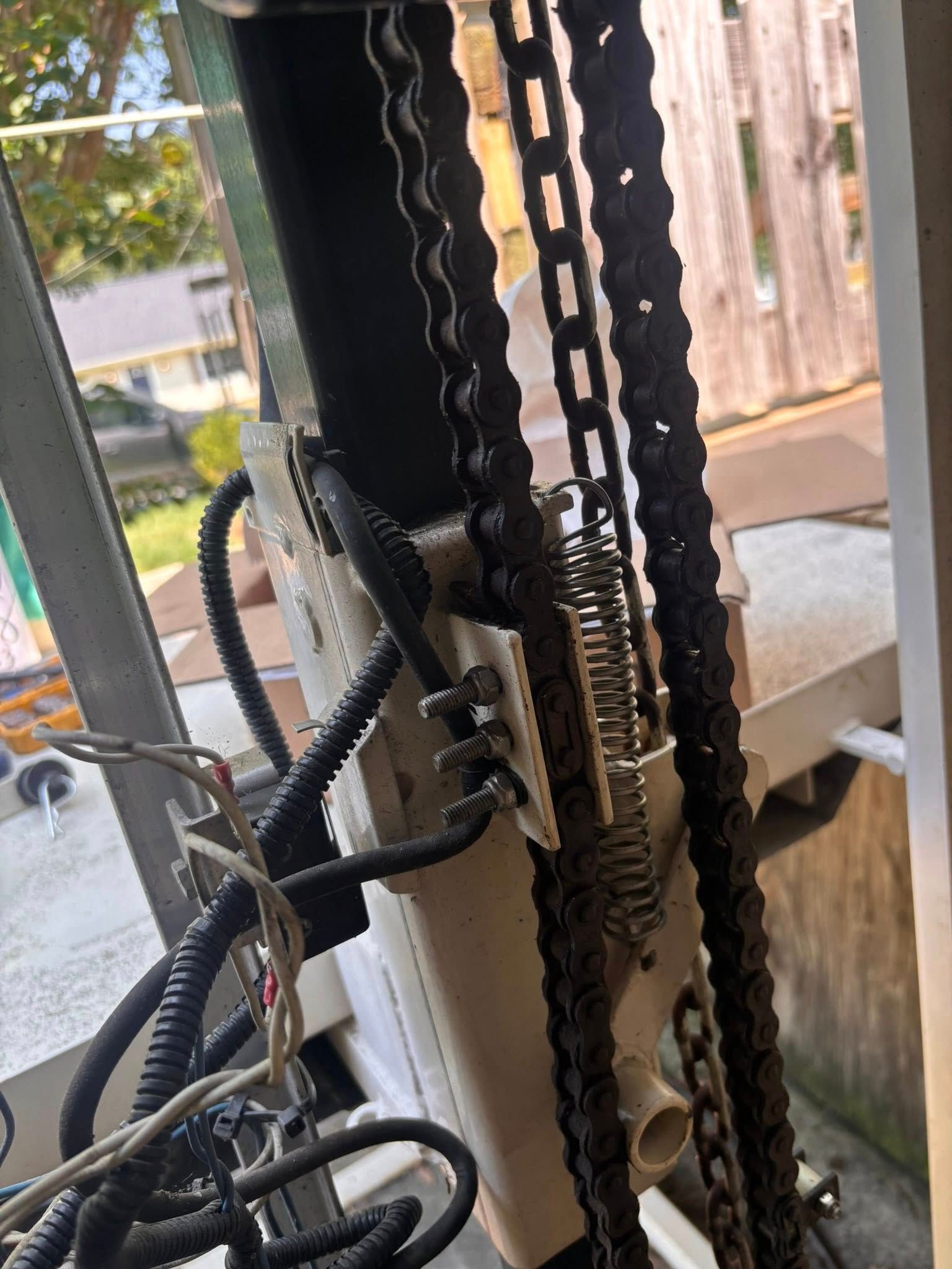 Chain and spring mechanism attached to a white support structure, possibly part of a lift or similar device, outdoors.