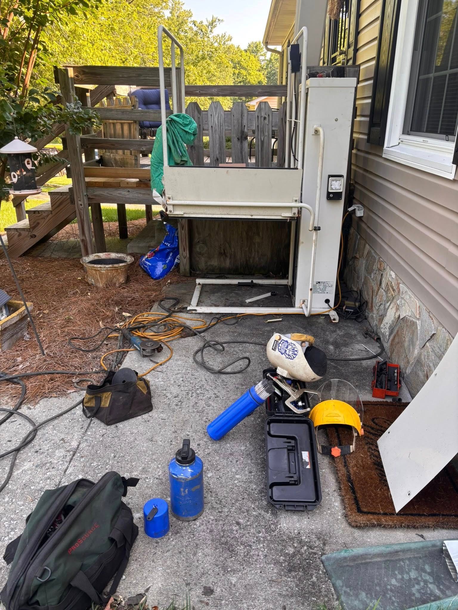 Outdoor wheelchair lift under construction next to a house with tools scattered around.