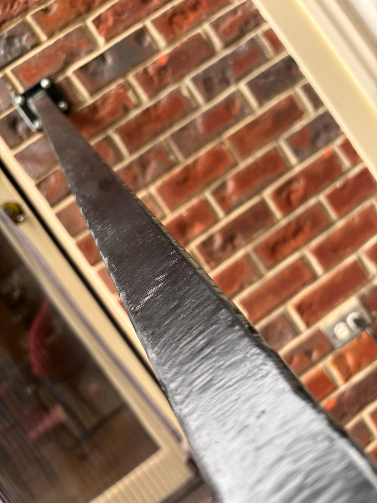 Close-up of a dark metal object with a jagged edge against a red brick wall.