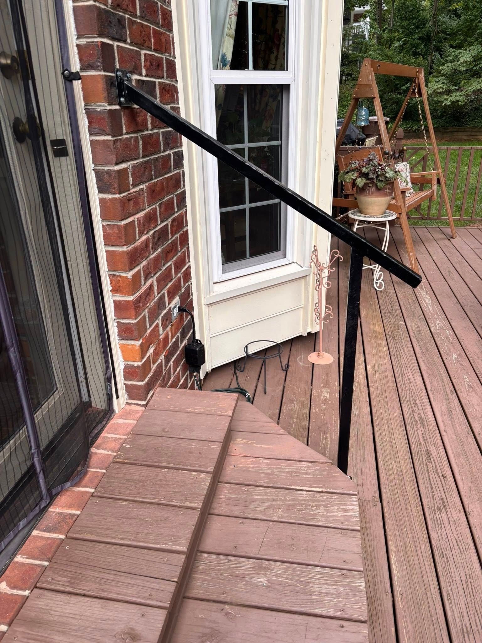 Black handrail on brick and wood deck steps. Window in the background.