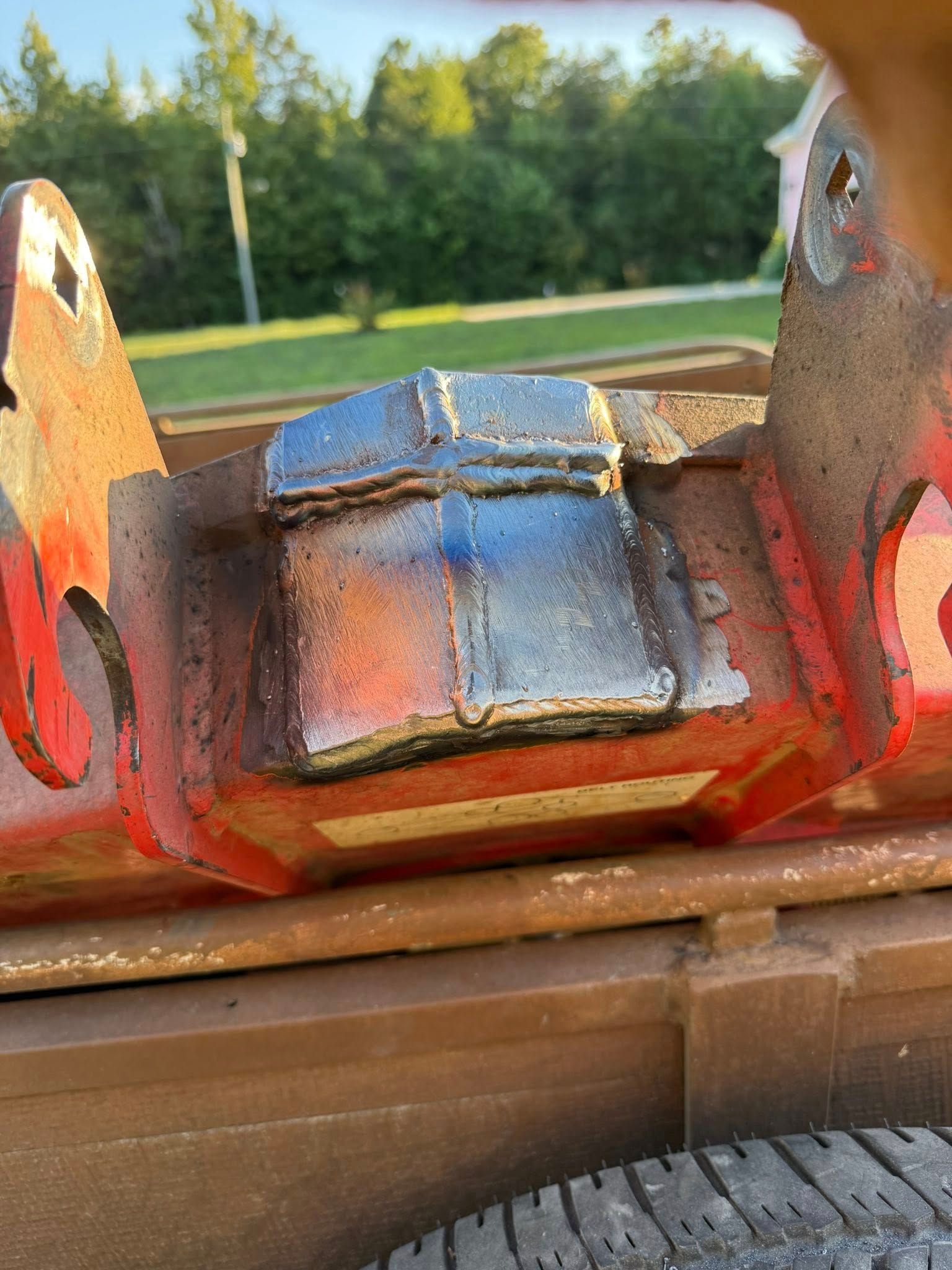 Welded metal repair on a red industrial equipment frame, outdoors.