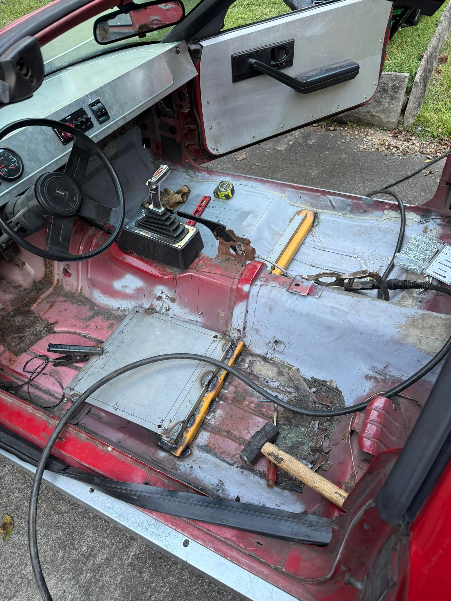 Red convertible car interior in process of restoration, metal panels, tools, exposed floor.