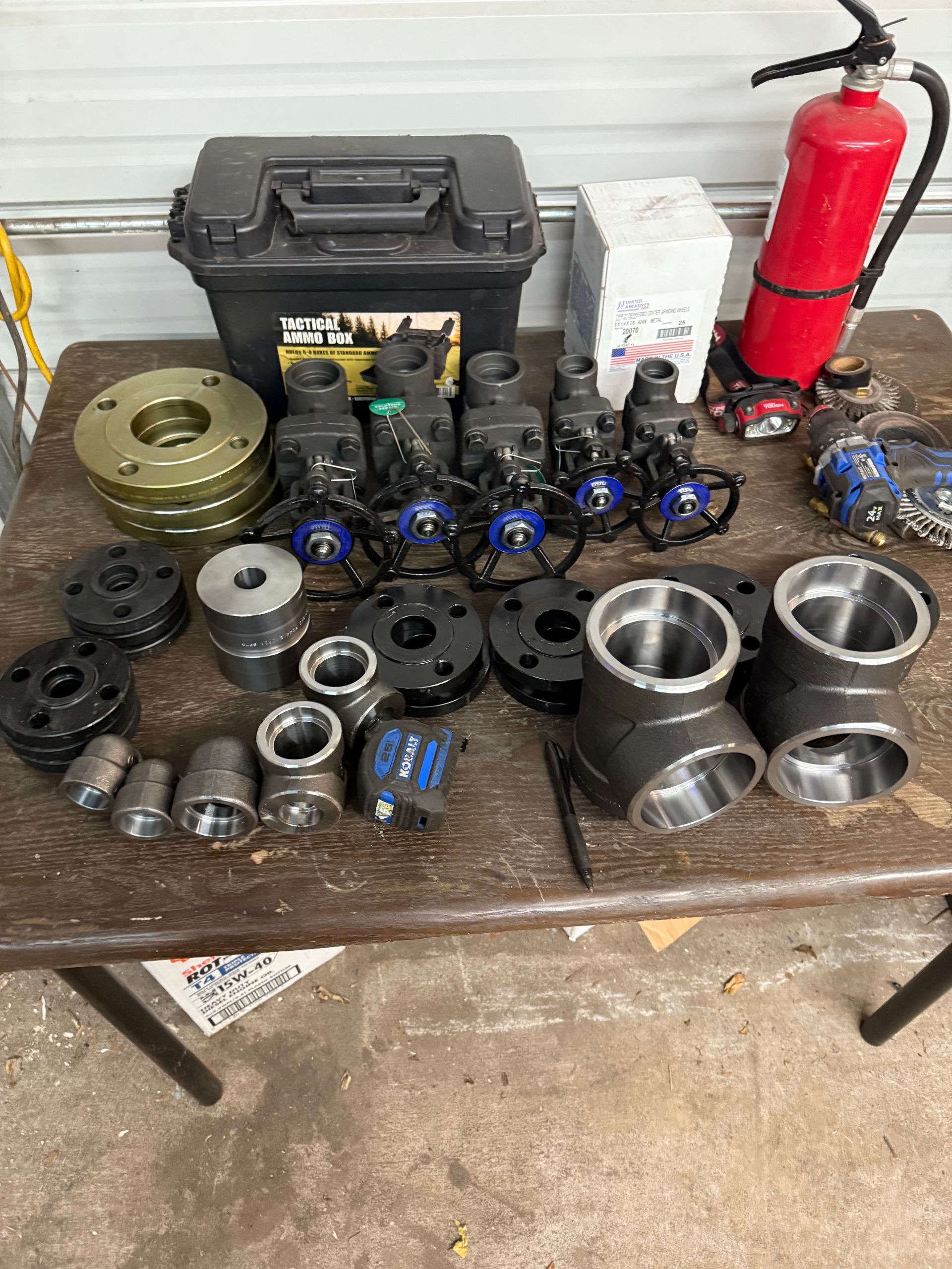 Various metal pipe fittings, valves, and a toolbox on a table, with a fire extinguisher.