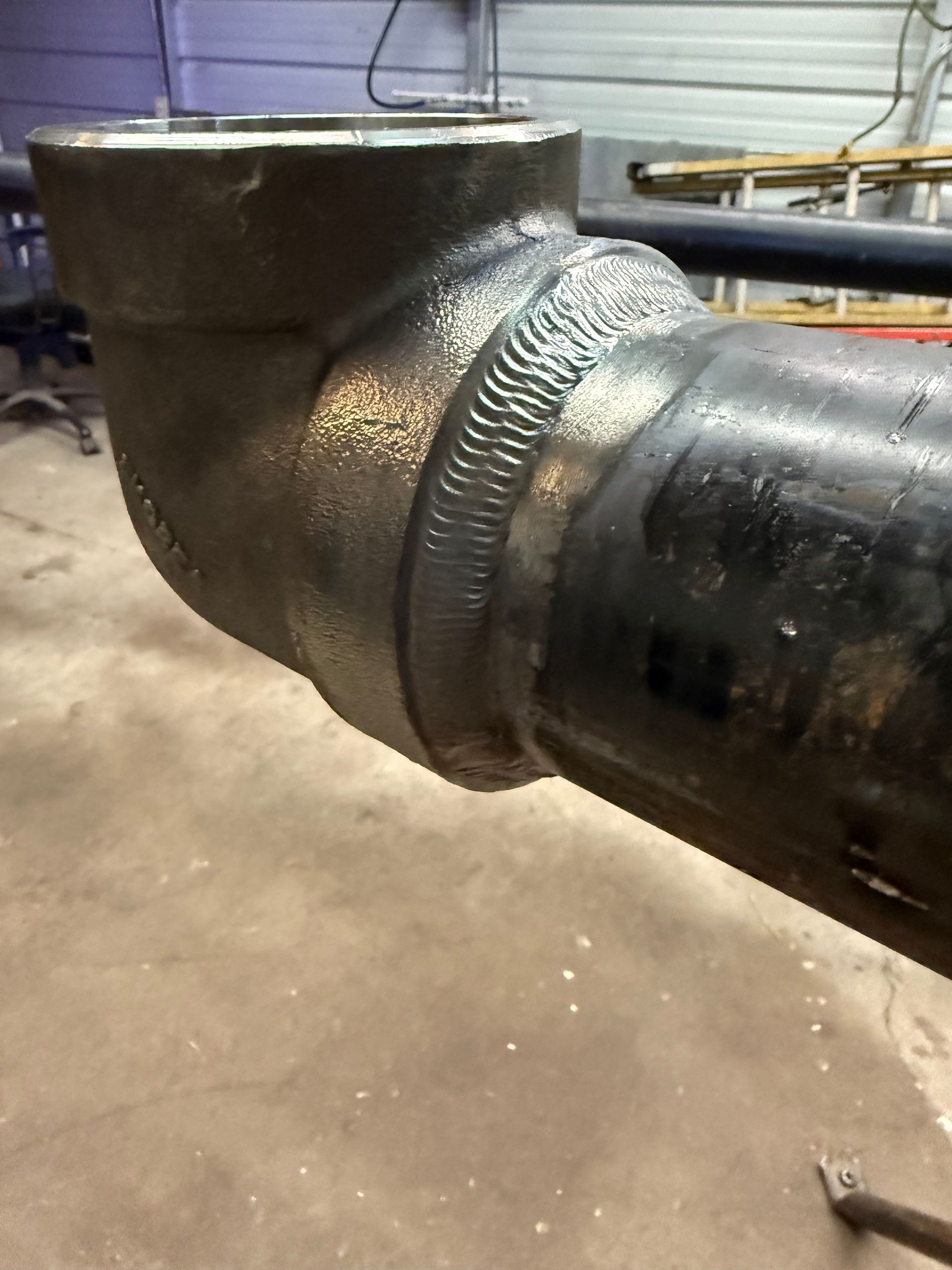Black pipe elbow welded to another pipe, indoors.