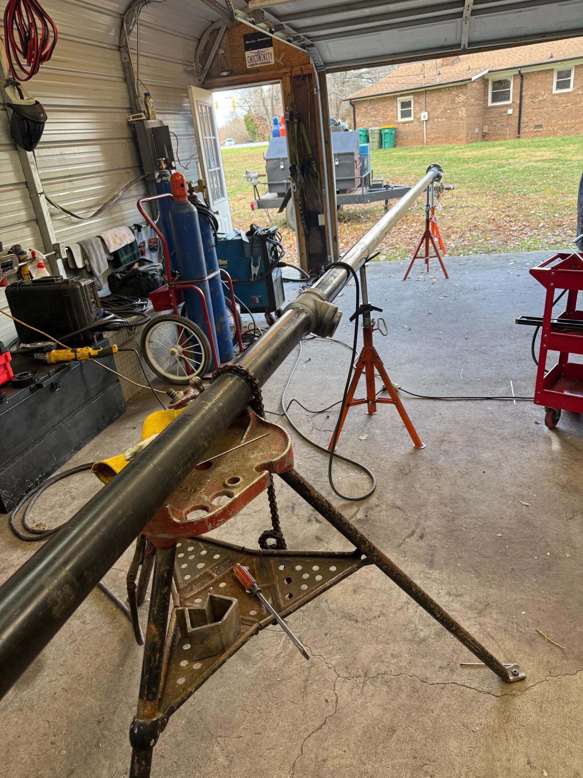 A long metal pipe is resting on a tripod and a sawhorse in a garage.