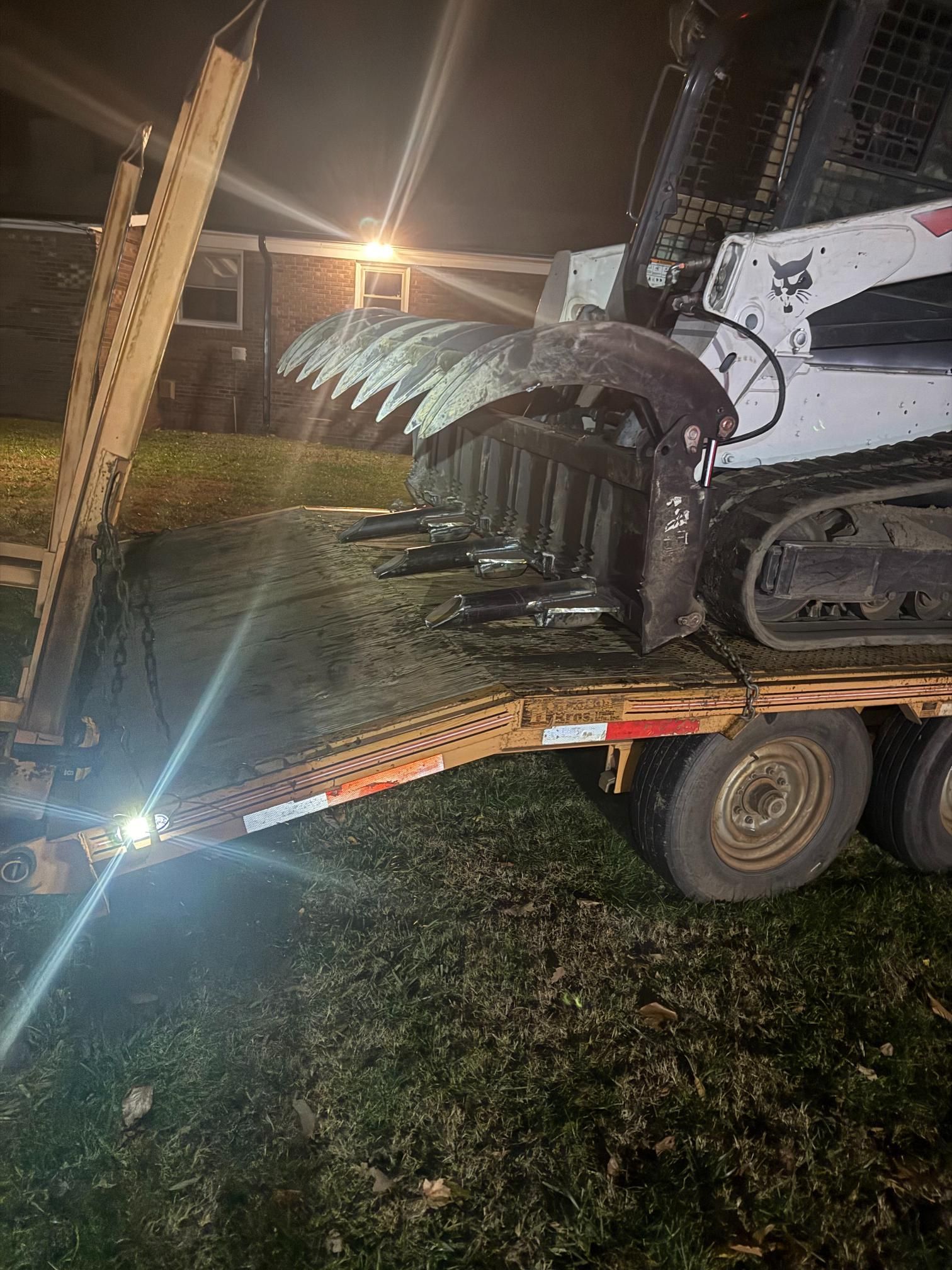 Bobcat skid-steer with a brush cutter attachment on a trailer at night.