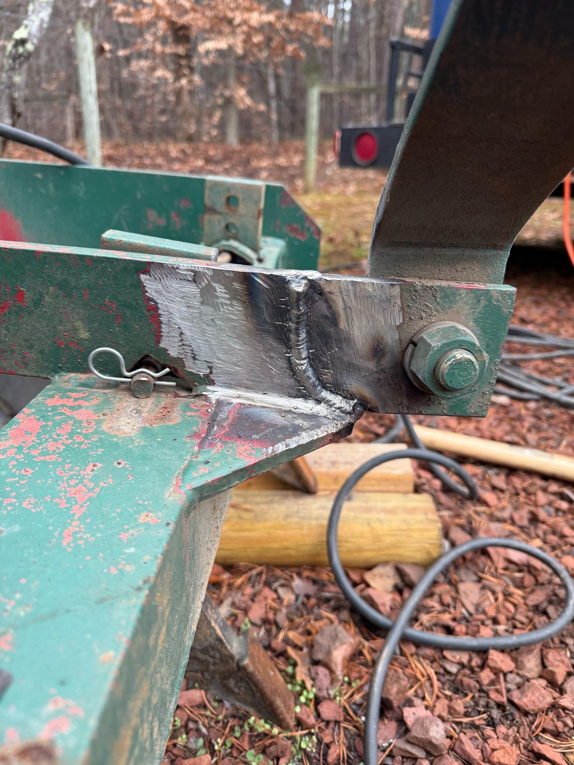 Welded metal repair on green farming equipment, visible bolt and cotter pin.