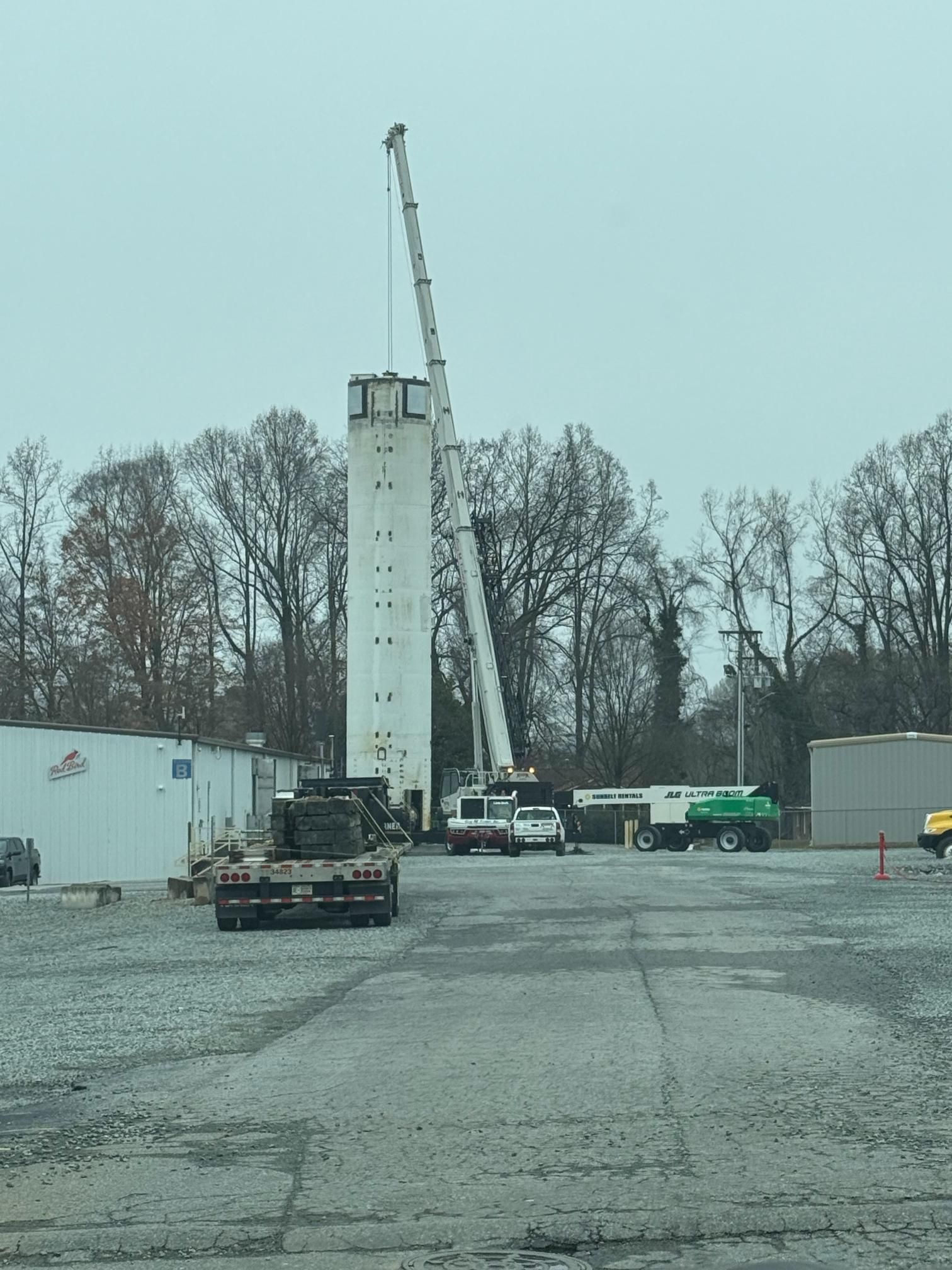 A tall white tower being worked on by a crane in an industrial setting.