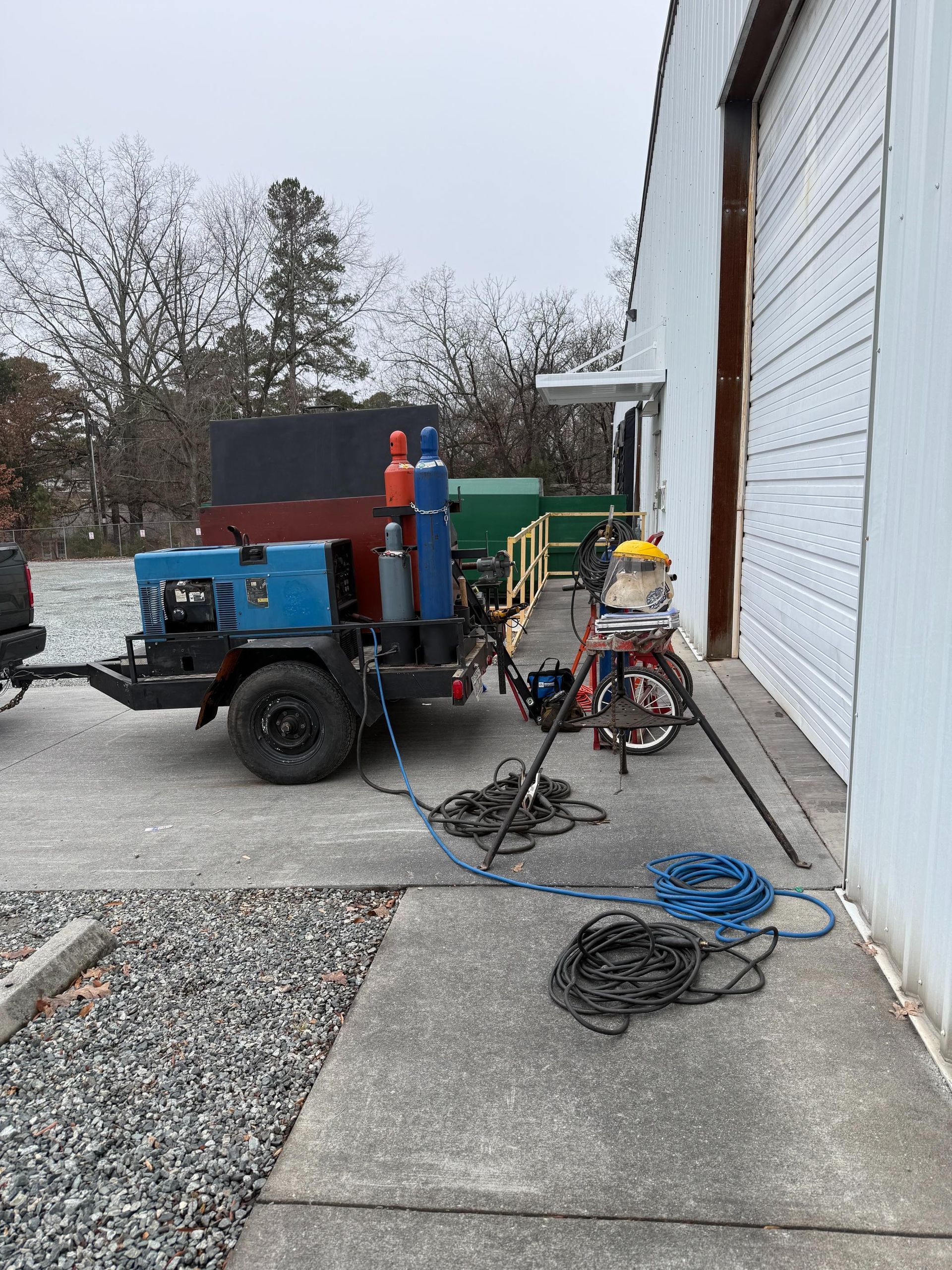 A welding trailer parked next to a building with cables and hoses on the ground.